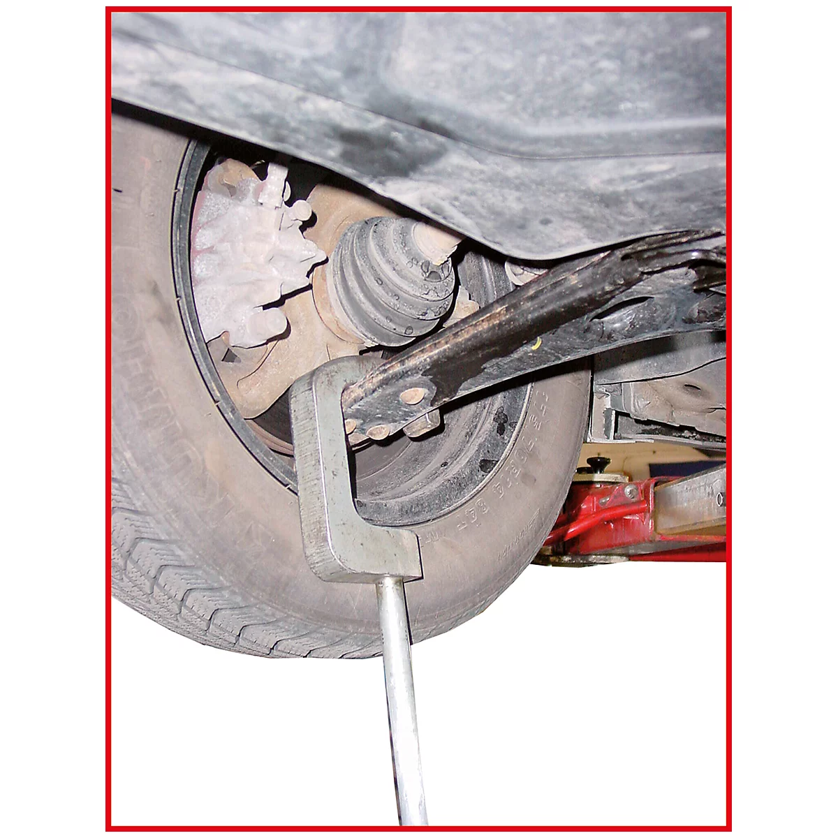 Nahaufnahme eines Autos von unten: Reifen, Achsschenkel und Spezialwerkzeug für die Wartung. Der Hintergrund ist weiß.